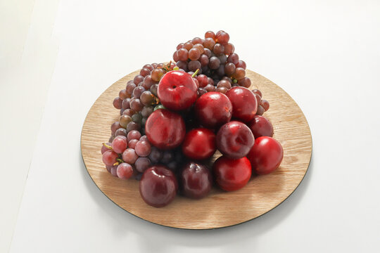 Cachos de uvas roxas e figos frescos sob um prato, isolados em um fundo branco.