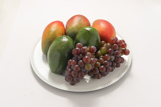 Cachos de uvas roxas e figos frescos sob um prato, isolados em um fundo branco.
