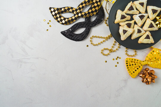 Purim holiday concept with carnival mask, party decoration and hamantaschen cookies on plate on bright background. Top view, flat lay