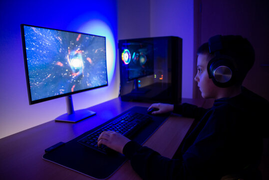 Young gamer focused on futuristic video game at desktop computer, immersive home gaming setup with rgb lighting and modern pc hardware