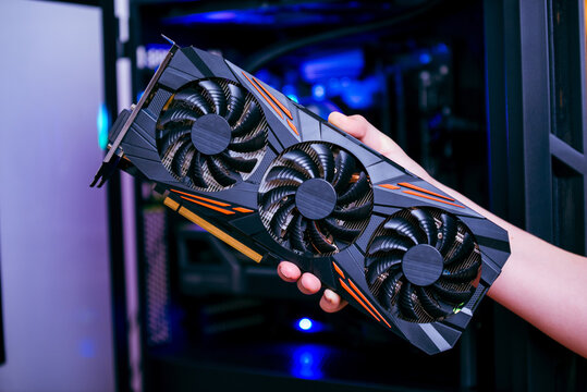 Hand holding powerful graphics card inside desktop pc, representing gaming performance, hardware upgrade and demand for high end gpu computing