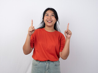 Happy young Asian woman in orange shirt and taupe pants is pointing the copy space above her, isolated by white background.