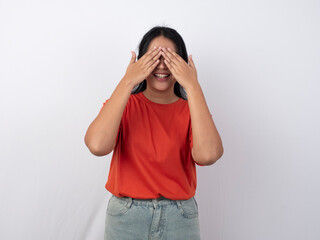 Charismatic and lovely Asian woman wearing an orange shirt, closing her eyes as if waiting for a surprise or making a peekaboo gesture, white background.