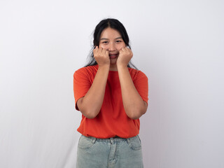 Young Asian woman in an orange T-shirt smiling at the camera with her hand covering her mouth, isolated on a white background.