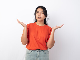 Shocked young Asian woman in an orange T-shirt with a surprised expression, pointing at copy space beside her, isolated on a white background.
