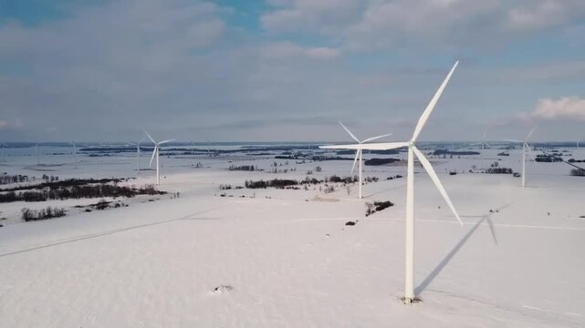Renewable wind turbines on a snowy winter beach generate green power from the sea breeze under a blue sky, showcasing sustainable energy technology within a beautiful coastal nature landscape