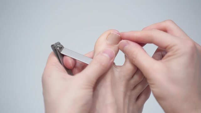 Man is cutting her nails on toes using nippers by herself, closeup view. Hygiene and care for feet.