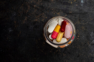 Various colorful prescription antibiotic capsules on jar bottle plastic onto a black background. Various colorful prescription capsule pills. Ideal for healthcare, pharmaceutical treatments