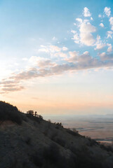 Obraz premium A gentle hillside overlooks an expansive landscape under a sky adorned with beautiful sunset clouds.