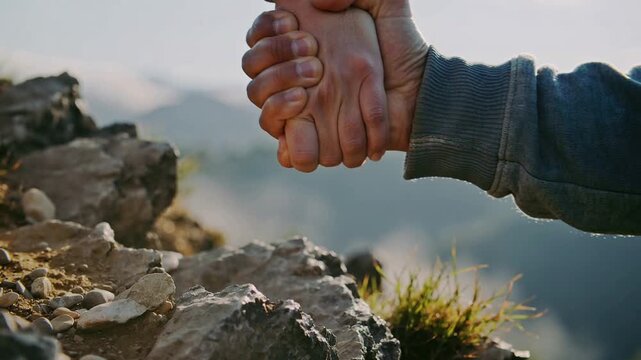 Helping hand reaching out to pull someone up a rocky mountain.