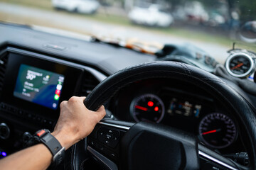 Close-up of Man Hand on Steering Wheel Driving a Modern Car,A close-up shot of a man's hand firmly gripping the leather steering wheel of a modern vehicle while driving. The image features a blurred