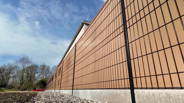 Smooth panning shot of a modern black rigid mesh fence with WPC composite wood privacy slat and concrete base outdoors.
