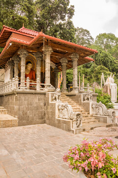 Seated Buddha inside a small pagoda accessed by stairs in the park of the Golden Temple of Dambulla