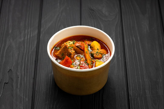 Hungarian bograch goulash soup with beef and vegetables in kraft bowl on dark wooden table
