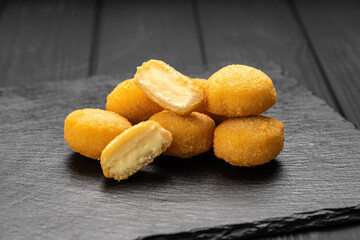 Crispy fried cheese bites with creamy filling on slate board, dark background
