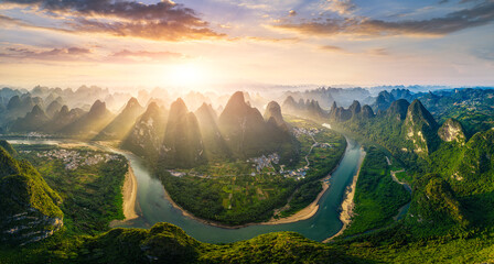Obraz premium Majestic aerial view of the winding Li River flowing through karst mountain peaks in Guilin, China during a golden sunrise with sun rays.