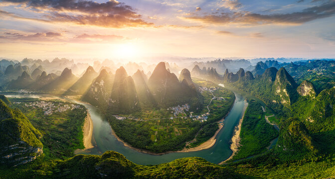 Majestic aerial view of the winding Li River flowing through karst mountain peaks in Guilin, China during a golden sunrise with sun rays.