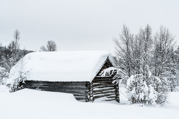 Old wooden building covered in snow in Sweden during winter season with trees surrounding it