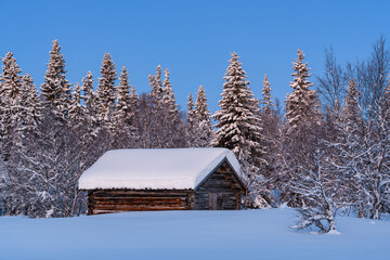 Old wooden building stands in snow covered forest in Sweden during winter season