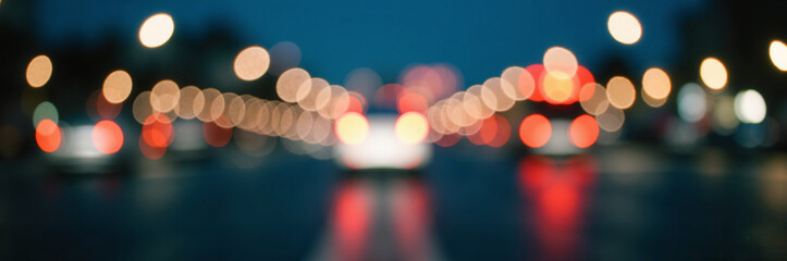 Blurred city street lights creating atmospheric glow at night, showcasing vibrant colors from vehicles and light reflections. Nighttime city view evokes sense of urban liveliness and movement.