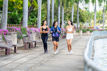 Fototapeta premium Three sporty women walking and talking by a riverside city promenade after workout. Active lifestyle, urban fitness, friendship, and healthy living with skyline background outdoors.