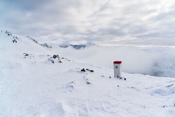 Open snow-covered ridge with hikers descending on the left side of the frame, beneath low-hanging clouds, while dense fog conceals the depth and scale of the mountain terrain, Tatra National Park