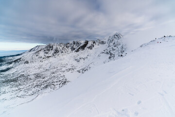 Tiny figures traverse a narrow snowy ridge surrounded by emptiness. The minimal composition highlights human scale against overwhelming alpine vastness and silence, Tatra national Park