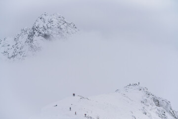 Tiny figures traverse a narrow snowy ridge surrounded by emptiness. The minimal composition highlights human scale against overwhelming alpine vastness and silence, Swinica, Tatra Mountains