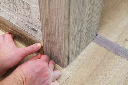 Installation of floor skirting boards and connecting thresholds on laminate flooring in the interior.