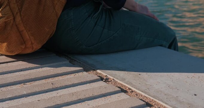 A person sits on a stone ledge by the water near Almudaina Palace, Majorca, Spain, on a sunny day.
