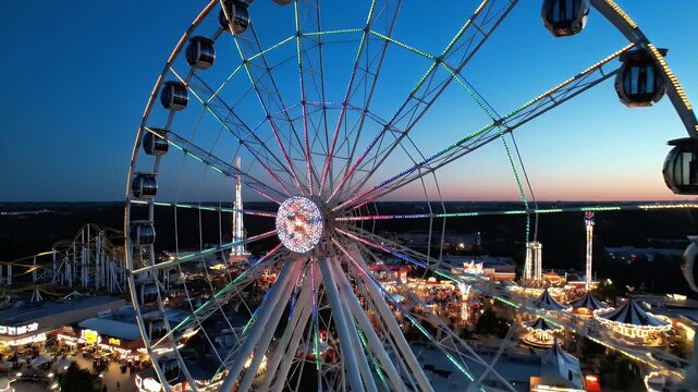 A brightly lit Ferris wheel dominates a vibrant night-time amusement park scene