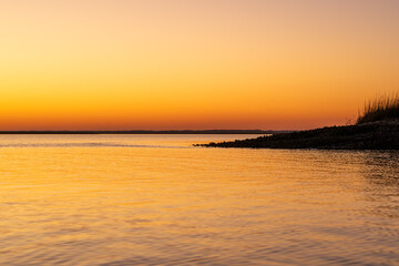 Obraz premium Sunset over the calm water at the shoreline of a river