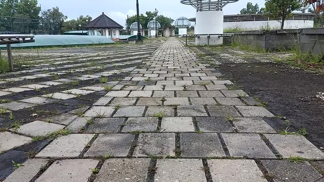 Low angle static shot of paving block walkway in outdoor sports center area with very light drizzle and wind moving grass.
