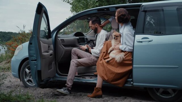 Young family with their pomeranian dog taking a selfie with a smartphone while sitting in their car