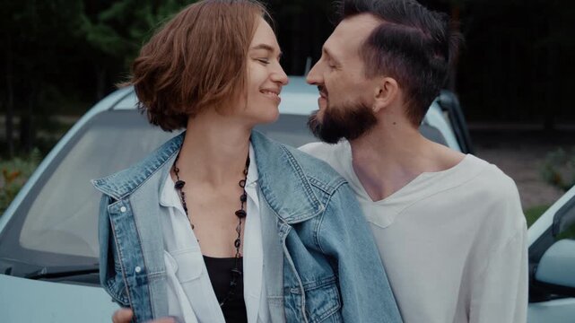 A young family sits together on the hood of their car, sharing hugs, laughter, and kisses during a memorable trip, surrounded by scenic travel views.