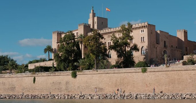 The historic Almudaina Palace in Palma de Mallorca, Spain, is captured from the calm water on a sunny day. Tilt shot.