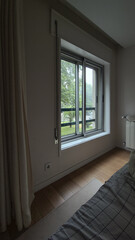 Fototapeta premium Cozy bedroom corner with an open window framing green trees outside, soft daylight falling on the bed and rug, suggesting a peaceful home retreat with a calming view.