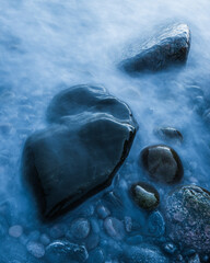 Stones and waves meet in the sea along the coast of Sweden during a cloudy day