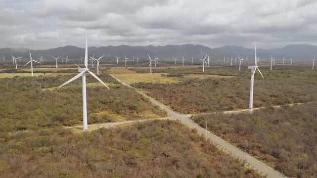 A renewable energy wind farm with powerful turbines and generators stands across a green rural landscape under a blue summer sky, providing clean electricity through sustainable technology