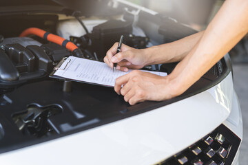 Fototapeta premium Auto check, car service shop concept. Automobile repairman writing job checklist on clipboard, mechanic checking engine to estimate repair machine, inspecting maintenance by engineer at vehicle garage