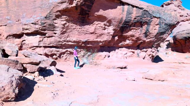 Panoramic shot following woman on dirt rail walking past tall red sandstone boulders and rugged cliffs with deep blue sky background
