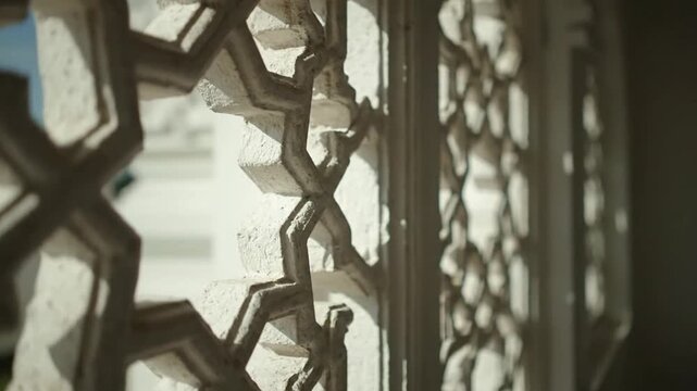 Intricate geometric lattice carved in white stone, architectural detail with sunlight casting shadows