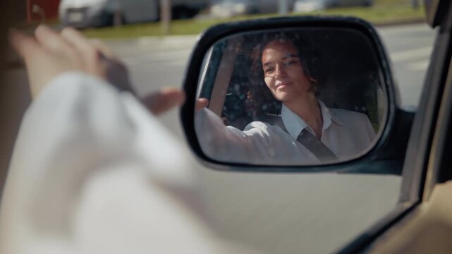 Young woman's face is reflected in a car's side-view mirror while driving in traffic
