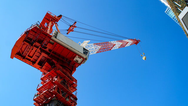 雲ひとつない青空の下で建設作業を行う赤と白の大型タワークレーン