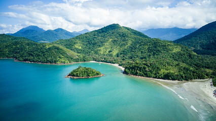 Diagonal aerial drone view of tropical coastline at Justa Beach with Maracujá Island visible in the scene, clear blue ocean water and natural vegetation on a sunny day. © Guga Asciutti