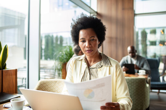 Businesswoman reviewing financial report at laptop in modern cafe