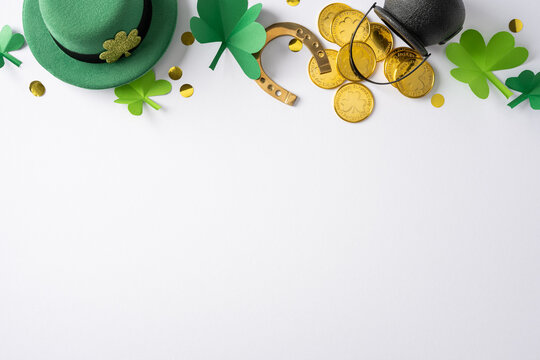 A festive flat lay with a green hat, shamrocks, gold coins, a horseshoe and glasses on a clean white background conveys luck, celebration and cheerful greeting for St Patrick's Day