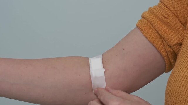 A woman presses a cotton pad to the puncture site after a blood test, medical examination, or blood donation.