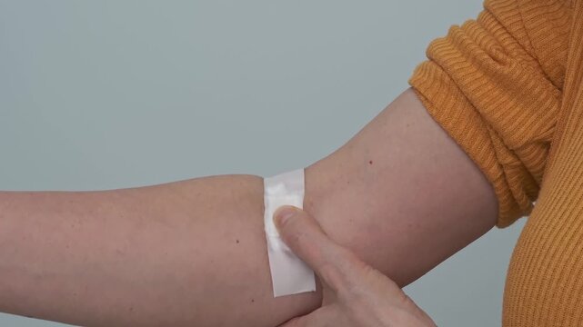 A woman presses a cotton pad to the puncture site after a blood test, medical examination, or blood donation.