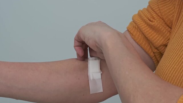 A woman removes a white bandage from her arm after a blood test or blood donation. Health check and blood donation concept.